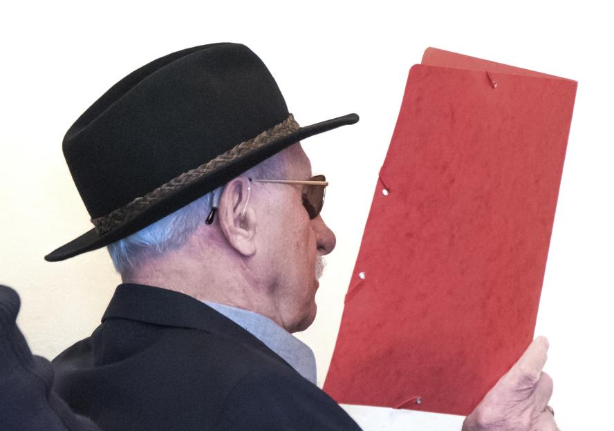 93-year-old former SS guard Bruno Dey in court, wearing a hat and sunglasses, holding a red folder.
