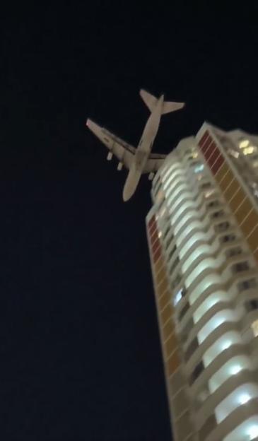 A large aircraft flying low over a tall building at night.