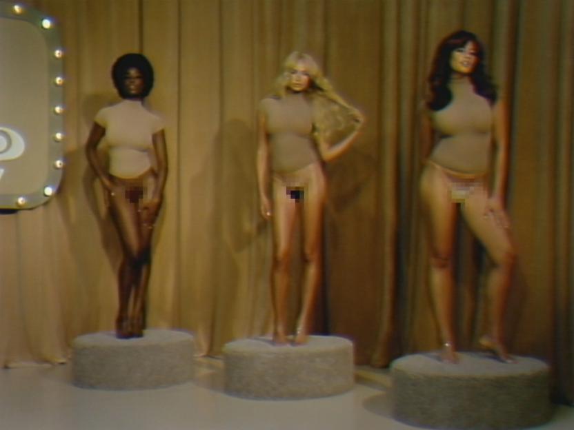 Three models on pedestals wearing skin-toned tops and pixelated sheer string thongs.