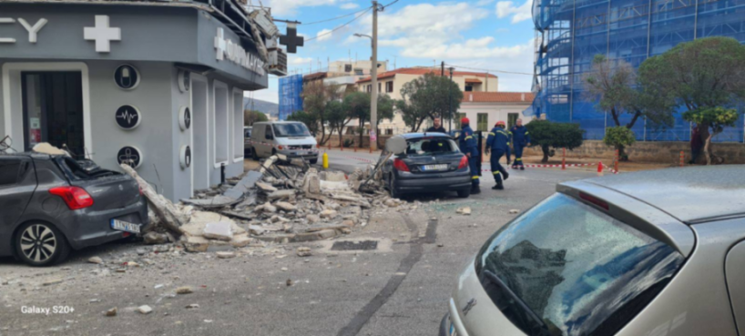 Debris from a damaged building on a street with cars and first responders.