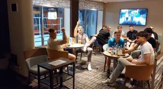 Group of men watching a sports game on TV in a lounge.