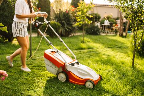 Woman mowing lawn with electric mower.
