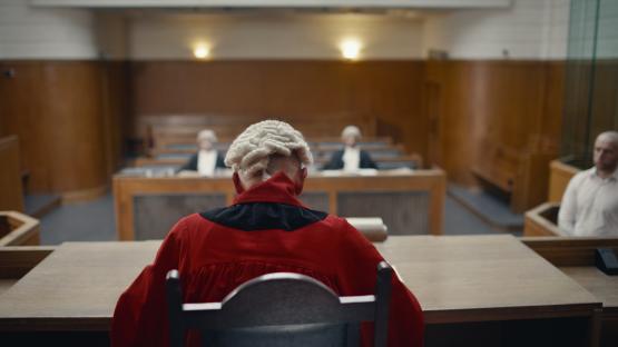 Judge in red robes sits in a courtroom.