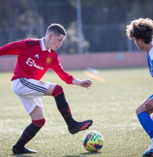 Soccer player in a Manchester United uniform dribbling the ball.