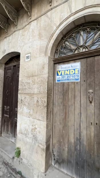 A weathered stone building with two wooden doors, one with a "Vende" sign indicating it is for sale.