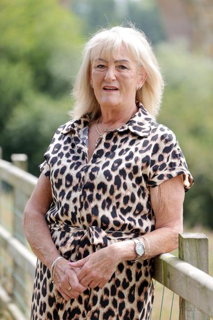 Maggie Rascal, a woman wearing a leopard print dress, leaning on a fence.
