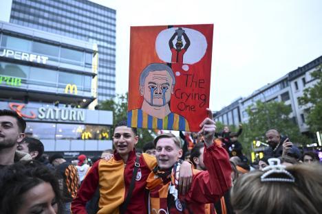 Galatasaray fans celebrating their Turkish Super Lig title victory, holding a sign depicting a crying man and a person holding a trophy.