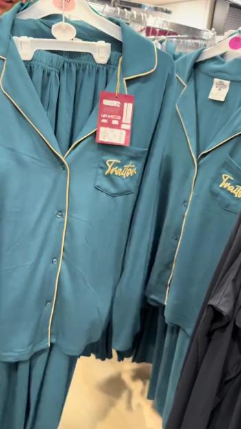 Teal pajamas with yellow piping and "Traitor" embroidered on the pocket, hanging on a rack.