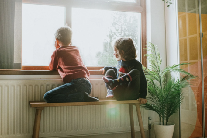 Two children sitting on a bench in front of a window.
