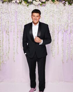 Man in tuxedo in front of floral backdrop.