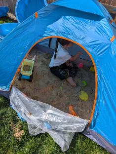 Child playing in a pop-up tent filled with sand.
