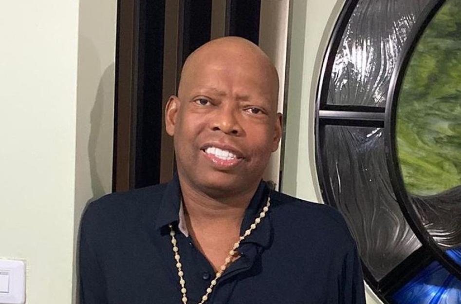 Faustino Asprilla, wearing a dark shirt and a beaded necklace, smiles at the camera.