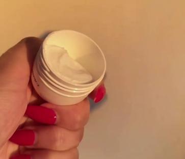 Hand holding open jar of cream.