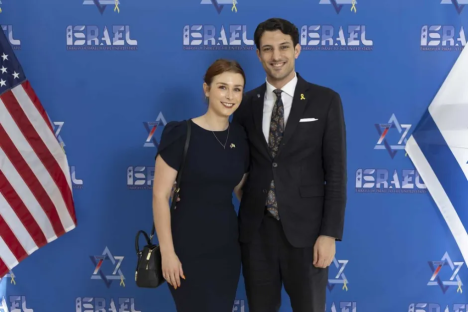 Couple posing in front of an Israeli flag and an American flag.