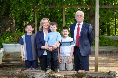 Family portrait of a woman, man, and three sons standing on a log.