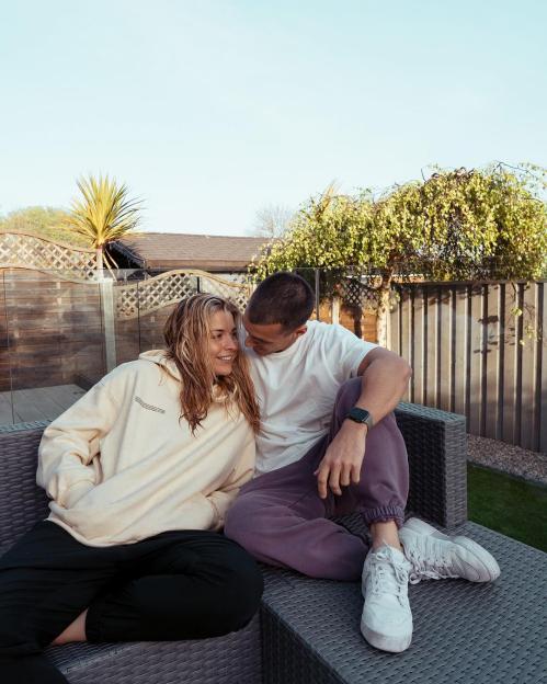 Maisie Smith sitting with Max George on a patio chair outdoors.