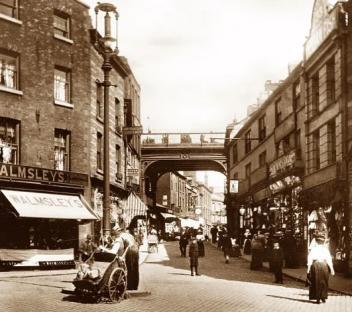 Sepia-toned photo of a street scene in Stockport, England, showing a covered walkway over the street.