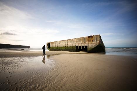Person standing on a beach looking at the remains of a concrete structure from WWII.