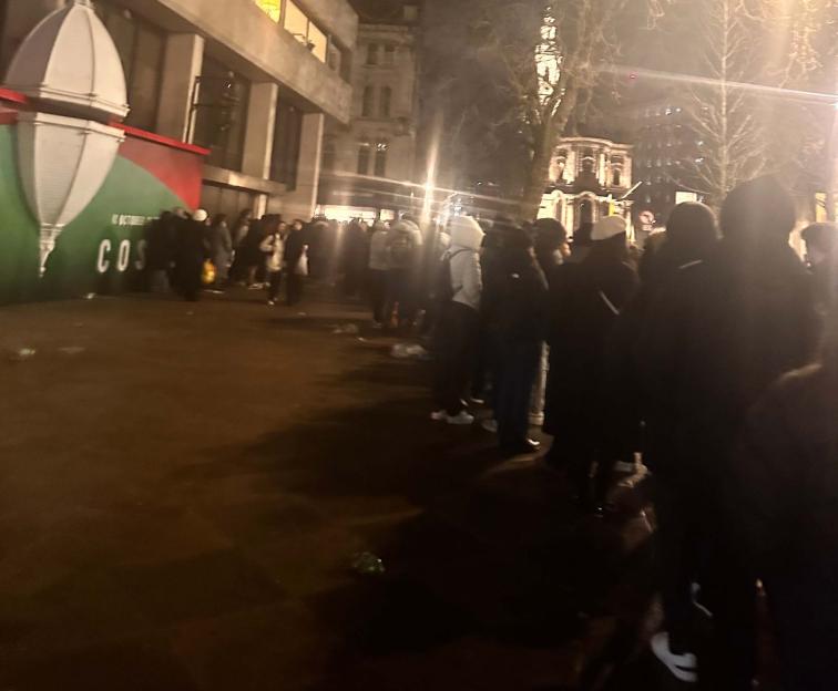 People in dark clothes gathered outside a building at night.