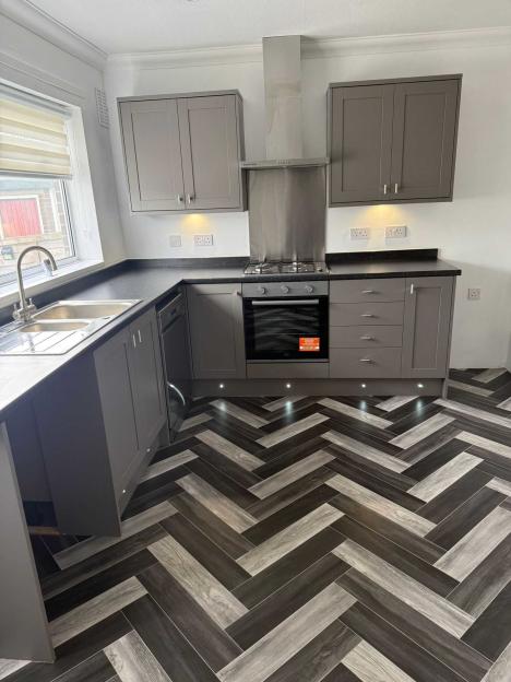 A modern kitchen with grey cabinets, dark countertops, and a herringbone floor.