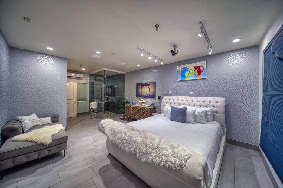 Bedroom with large bed, chaise lounge, and glass shower.