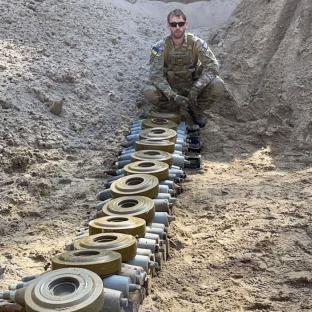 A bomb disposal expert sits amidst a row of Russian munitions.