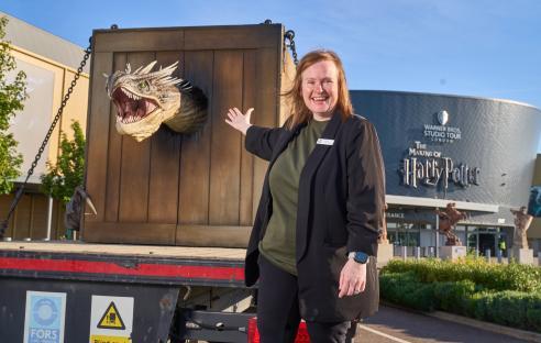A woman stands next to a large animatronic dragon head on a truck, in front of the Warner Bros. Studio Tour London â The Making of Harry Potter.