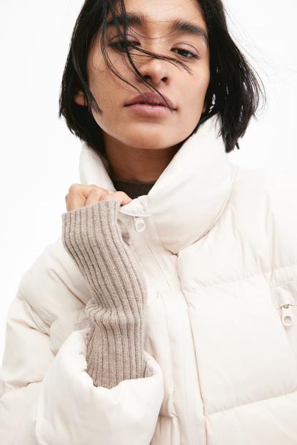 A model wearing a cream-colored puffer jacket and beige rib-knit wrist warmers.