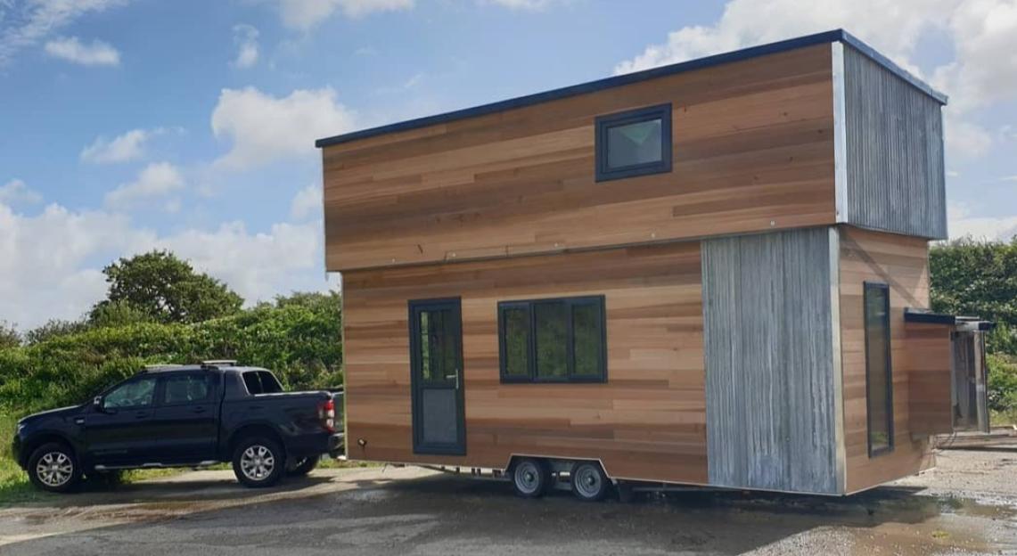 A black truck towing a large, modern wooden tiny house on wheels.