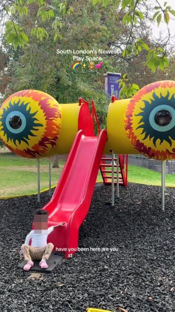 A child sitting at the bottom of a red slide in a playground with eye-shaped structures.