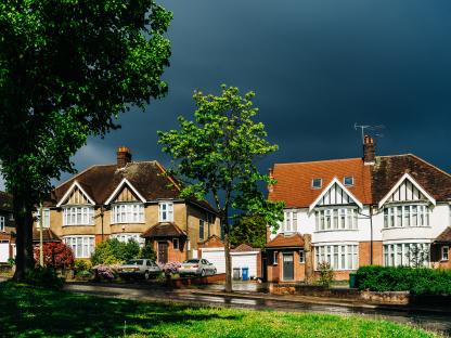 Two houses on a sunny day with dark clouds.