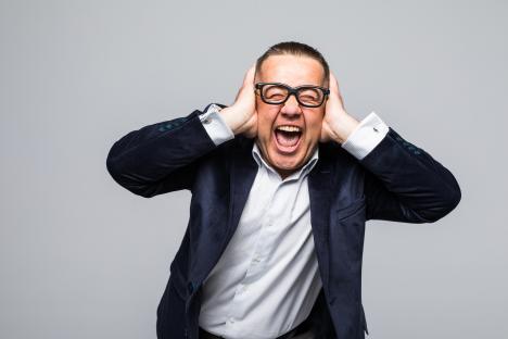 A man in a suit screaming with his hands over his ears.