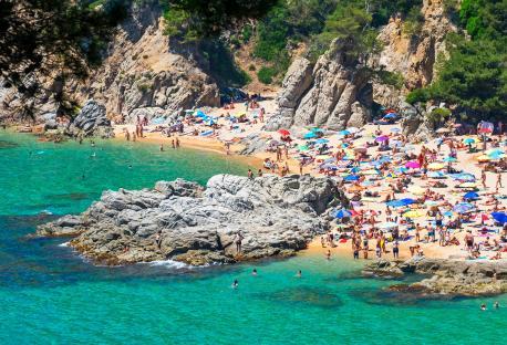 Crowded naturist beach with colorful umbrellas.