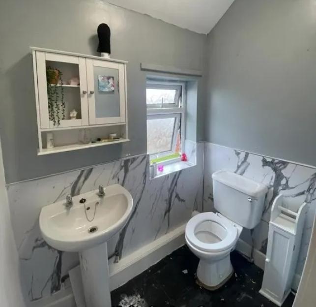 Before photo of a small bathroom with gray walls, a pedestal sink, and a toilet.
