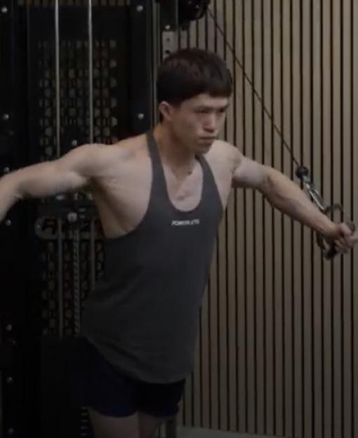 Man in a gray tank top working out on a cable machine.