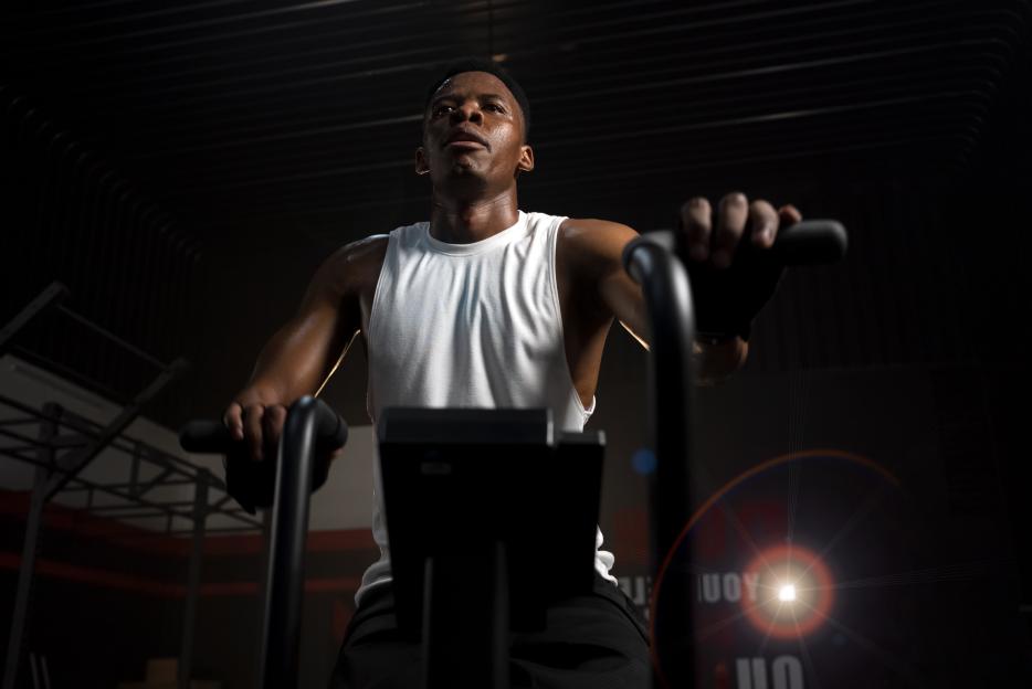 Sweaty man in white tank top doing cardio on an exercise machine.