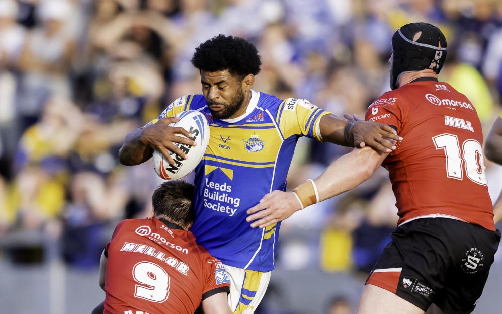 Leeds Rhinos player Rhyse Martin runs with the ball while being tackled by Salford Red Devils players.