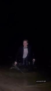 Man in tuxedo wading in dark water.