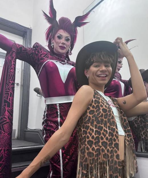 A person in drag queen attire with a spiky red wig and a person in a leopard print vest and cowboy hat.