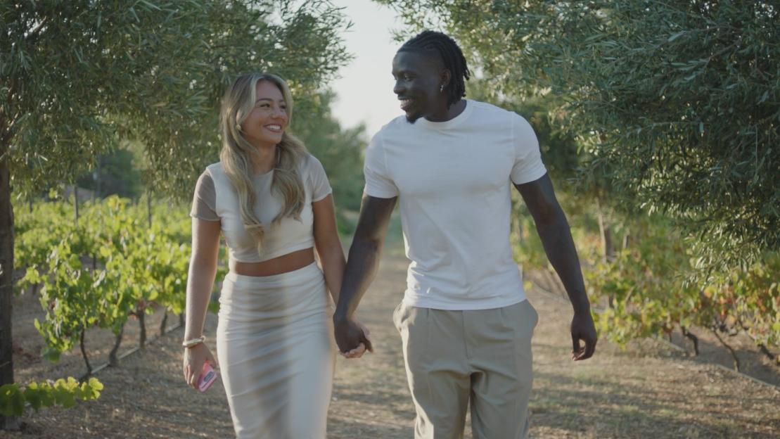 Shakira and Conor holding hands and walking in a vineyard.