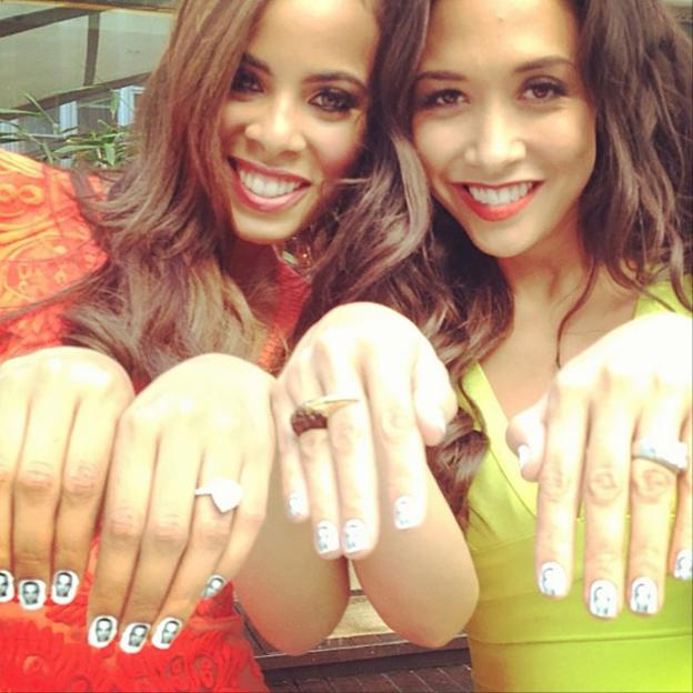 Two women showing off their nails with small images on them.