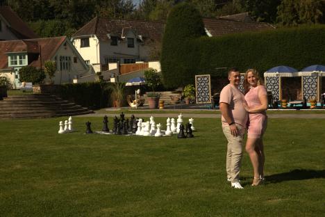 Couple standing on a lawn with a giant chessboard in the background.