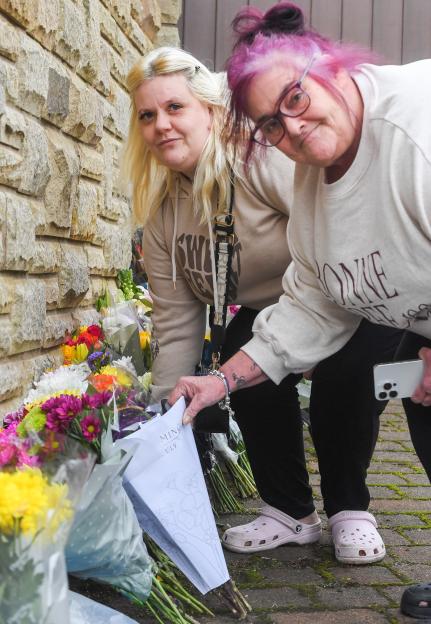 Two women, Kirsty and Lisa Cartwright, placing flower tributes outside a stone building.