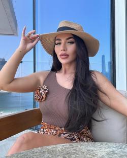 Woman in brown top and leopard print skirt wearing a straw hat.