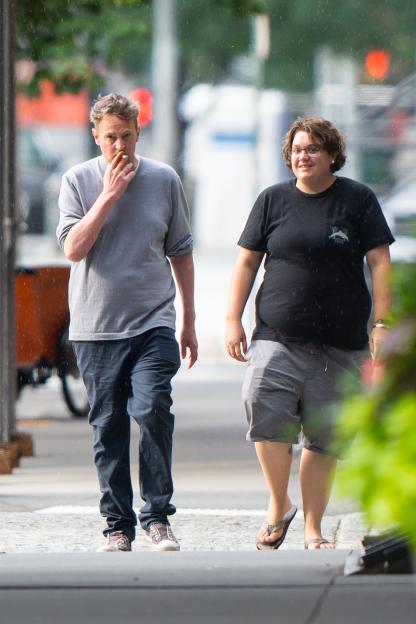 Matthew Perry smoking while walking with a friend in the rain.