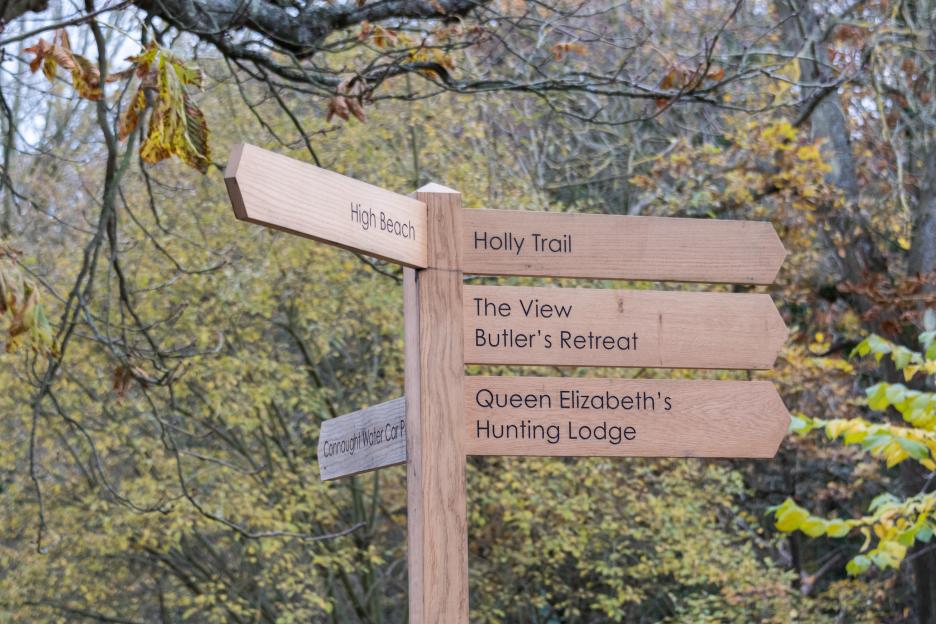 A wooden signpost pointing to "High Beach," "Connaught Water Car Park," "Holly Trail," "The View," "Butler's Retreat," and "Queen Elizabeth's Hunting Lodge."
