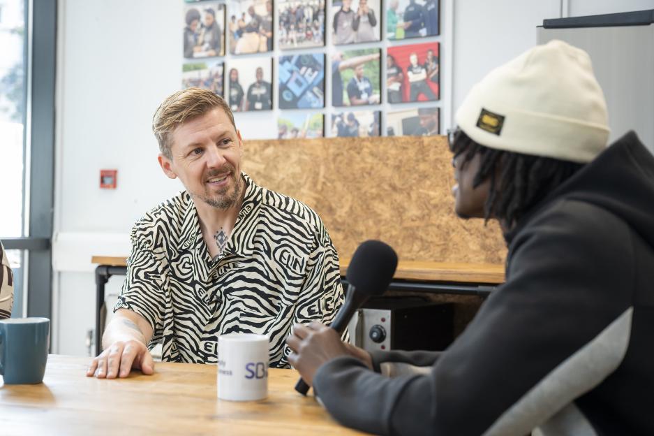 Two people sitting at a table, one holding a microphone.