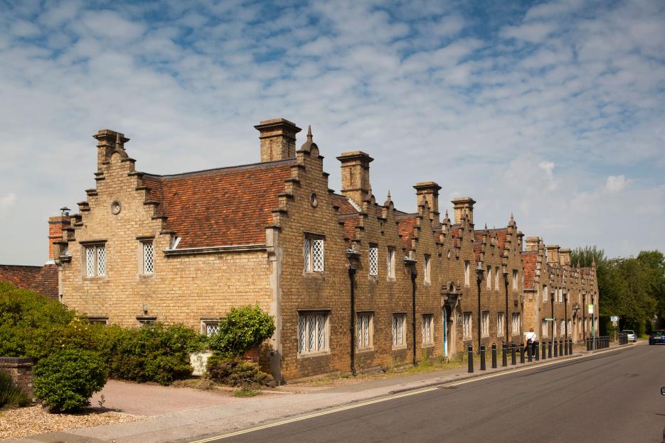 A long row of historic almshouses in Woburn, Bedfordshire, with ornate gables and chimneys.