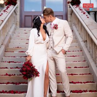 A couple kissing on a staircase covered in rose petals.