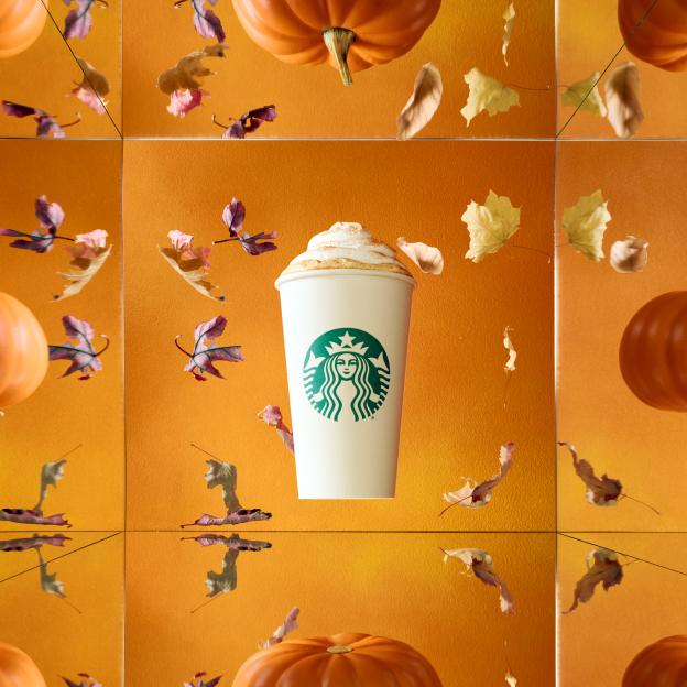 A Starbucks pumpkin spice latte with whipped cream and cinnamon surrounded by falling autumn leaves and pumpkins.
